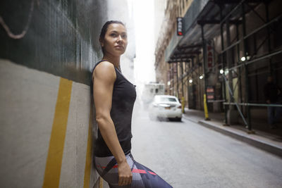 Side view of thoughtful sporty woman leaning on wall by street