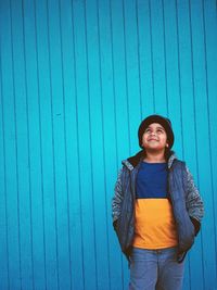 Portrait of smiling young woman standing against blue wall