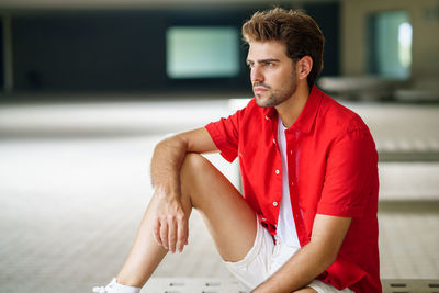 Young man looking away sitting on bench in building