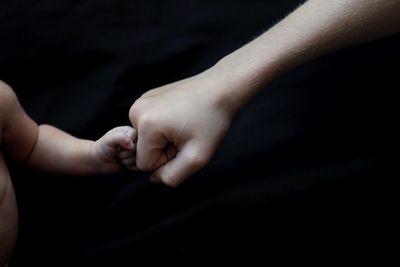 Close-up of mother and baby bumping fist over black background