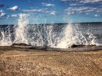 Waves breaking on beach against sky