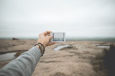 Close-up of hand holding smart phone against sky