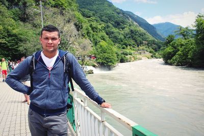 Portrait of smiling man standing on footbridge over river