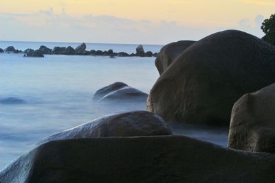 Rocks by sea against sky during sunset