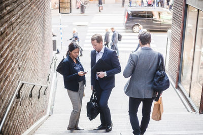 Male and female coworkers using phone on staircase in city