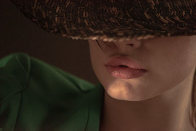 Close-up of woman covering eyes with hat against colored background