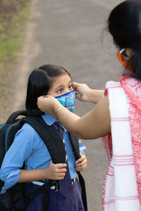 An indian school girl child going to school again after pandemic with her mother wearing nose mask 