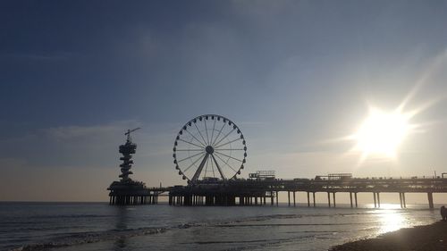 Ferris wheel by sea against sky at sunset