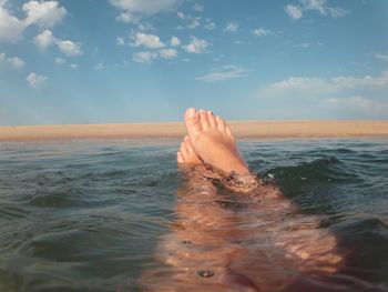 Low section of person swimming in sea against sky