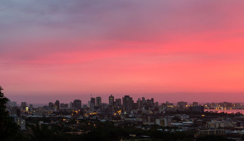 Illuminated cityscape against sky at sunset