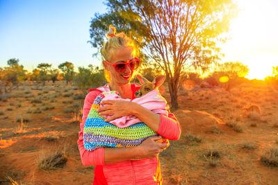 Smiling woman holding kangaroo on field during sunset