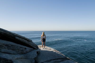 View from behind of a woman standing on the cliff overlooking the ocean