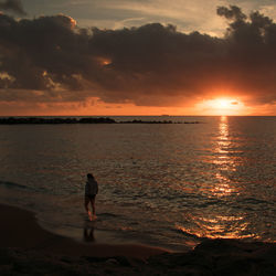 Silhouette person on beach against sky during sunset