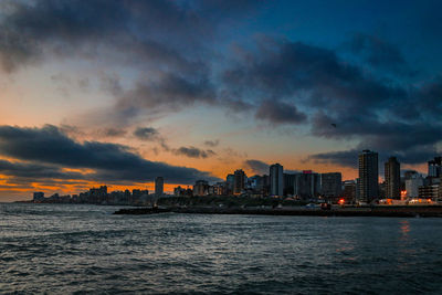 Sea by buildings against sky during sunset