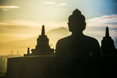 Silhouette of buddha statue against cloudy sky