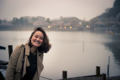 Portrait of smiling young woman standing by lake against sky