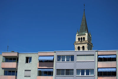 Low angle view of new building with church in background against clear blue sky