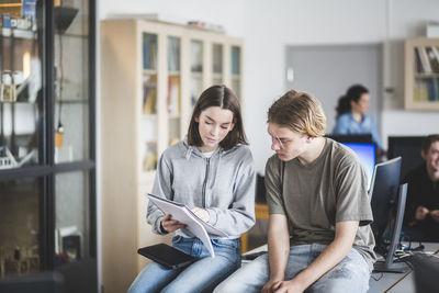 High school students studying from book while sitting on desk in computer lab