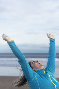 Happy woman raising arms on the beach in winter