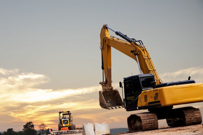 Earth mover at construction site against sky during sunset