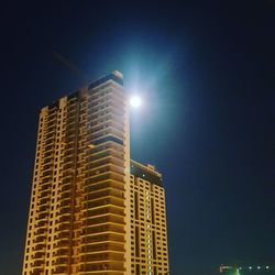 Low angle view of illuminated skyscrapers against blue sky