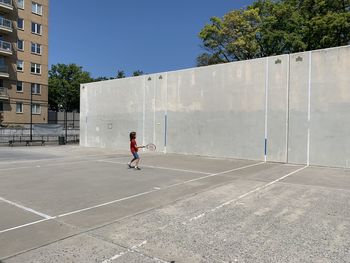 Boy playing tennis in city against laege concrete wall with blue sky 