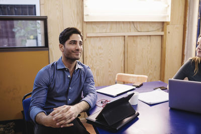 Smiling young man looking away while sitting at desk in office