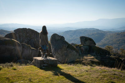 Caucasian young woman with brown dog on top of a boulder stone seeing sortelha landscape