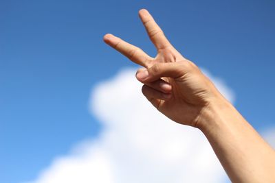 Cropped hand gesturing peace sign against sky