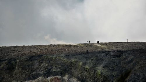 Low angle view of people on cliff against sky