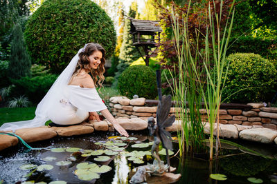 Young woman sitting by plants against trees