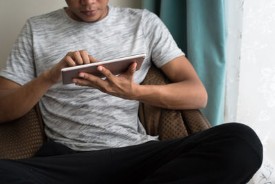 Midsection of man using mobile phone while sitting on sofa at home