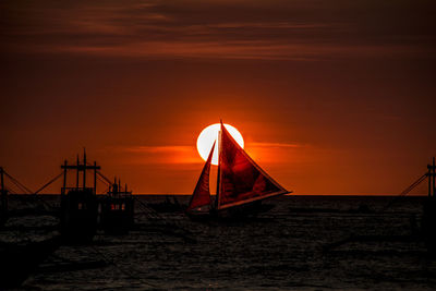 Silhouette of sailboat in sea at sunset