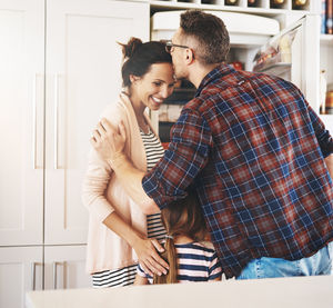 Man kissing woman forehead standing by daughter at home