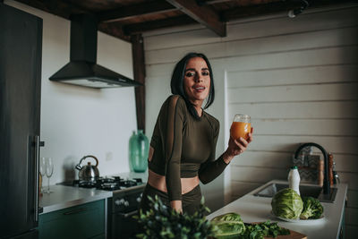 Portrait of smiling woman standing in kitchen at home