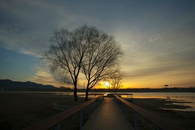 Pier by lake against sky during sunset