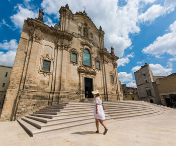 Rear view of woman walking by church against cloudy sky