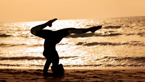 Silhouette man with arms raised on beach against sky during sunset