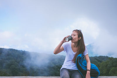 Young woman using phone while standing on mountain against sky