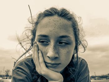 Close-up of thoughtful teenage girl against cloudy sky