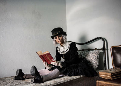 Portrait of young woman sitting on book against wall