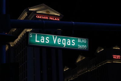 Low angle view of road sign against illuminated city at night
