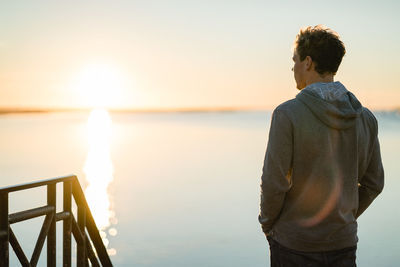 Rear view of man standing against sea during sunset