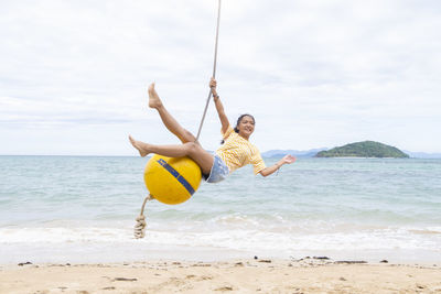 Rear view of woman swinging at beach against sky