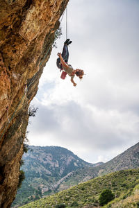 From below fearless young female alpinist enjoying climbing and adrenaline while hanging upside down from cliff