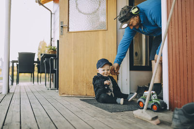 Smiling father playing with son sitting on doormat at porch