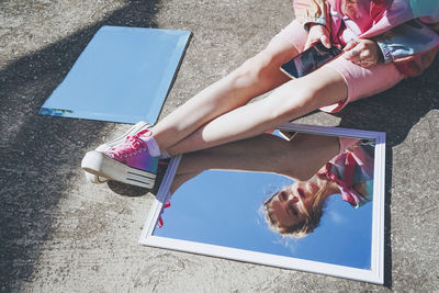 Reflection of woman using smart phone sitting on road by mirrors