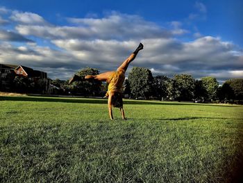 Woman practicing cartwheel at park against sky