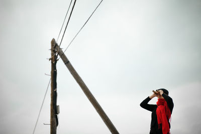 Low angle view of woman looking through binoculars while standing against sky