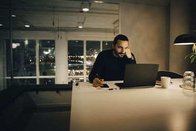 Tired businessman working late while sitting at desk in illuminated creative office